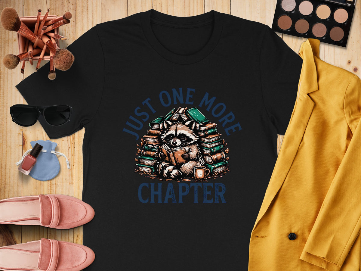 Black t-shirt with raccoon reading surrounded by books, text "JUST ONE MORE CHAPTER."