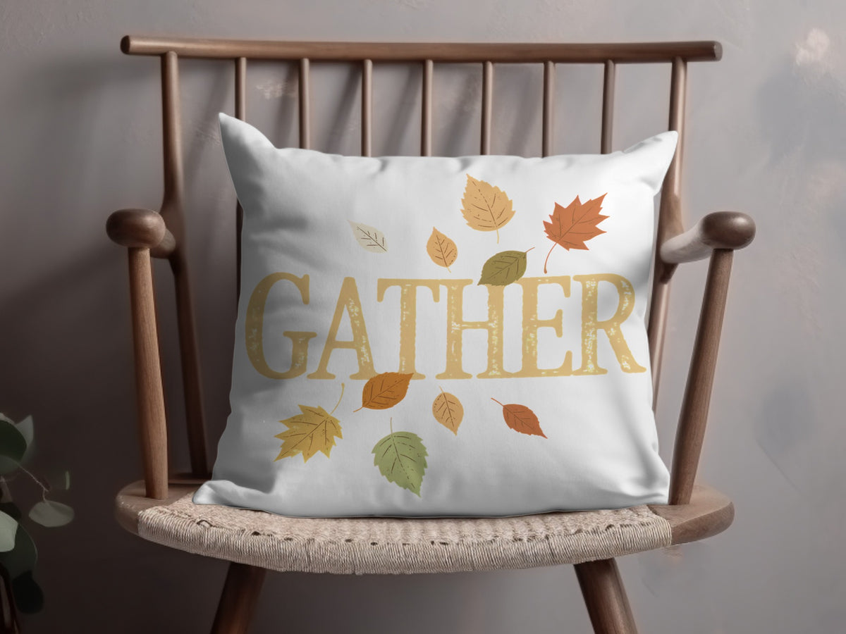 White pillow with "GATHER" text and falling autumn leaves on wooden chair.