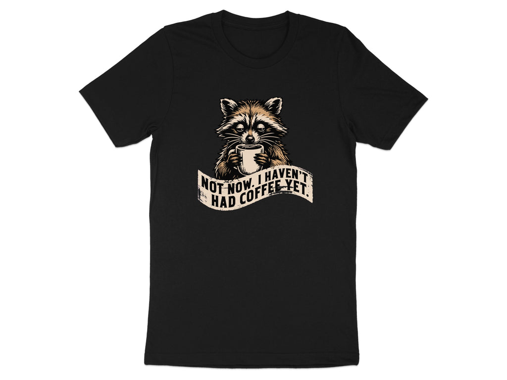 Black t-shirt featuring a raccoon holding a coffee cup with text "Not now. I haven't had coffee yet."