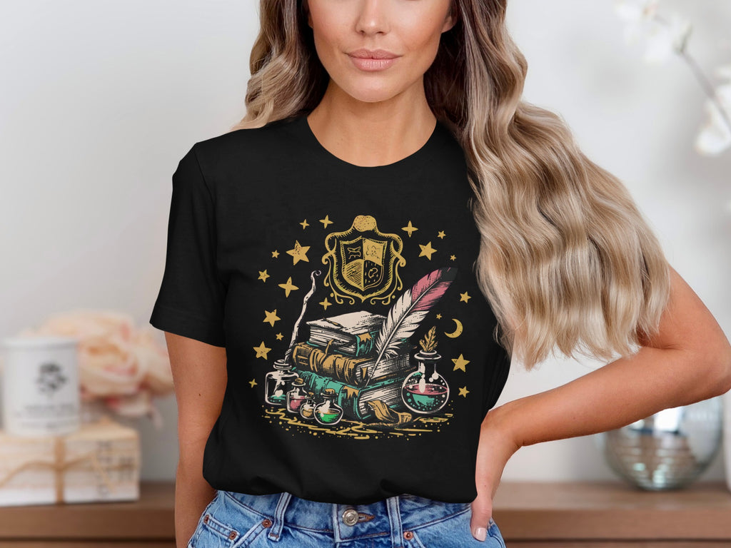 Black t-shirt with a whimsical illustration of books, potions, and a quill, surrounded by stars.