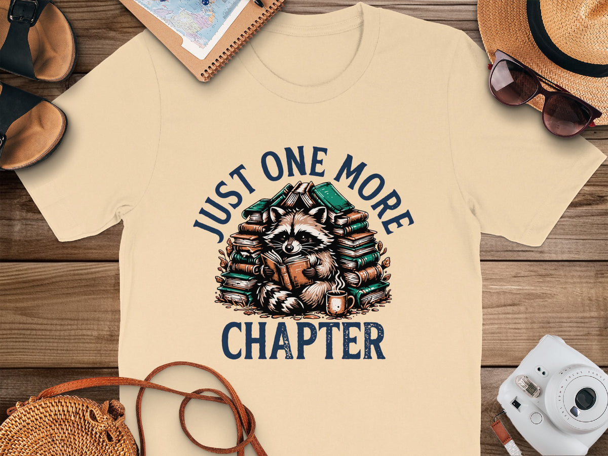 T-shirt with raccoon reading books and text "JUST ONE MORE CHAPTER."