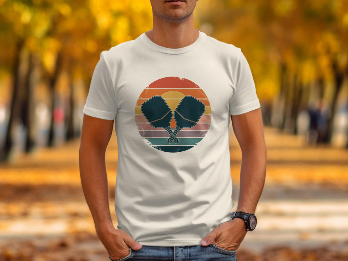 White t-shirt featuring crossed pickleball paddles on a distressed circular sunset graphic.