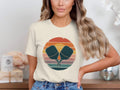Cream t-shirt with crossed pickleball paddles in a retro sunset graphic.