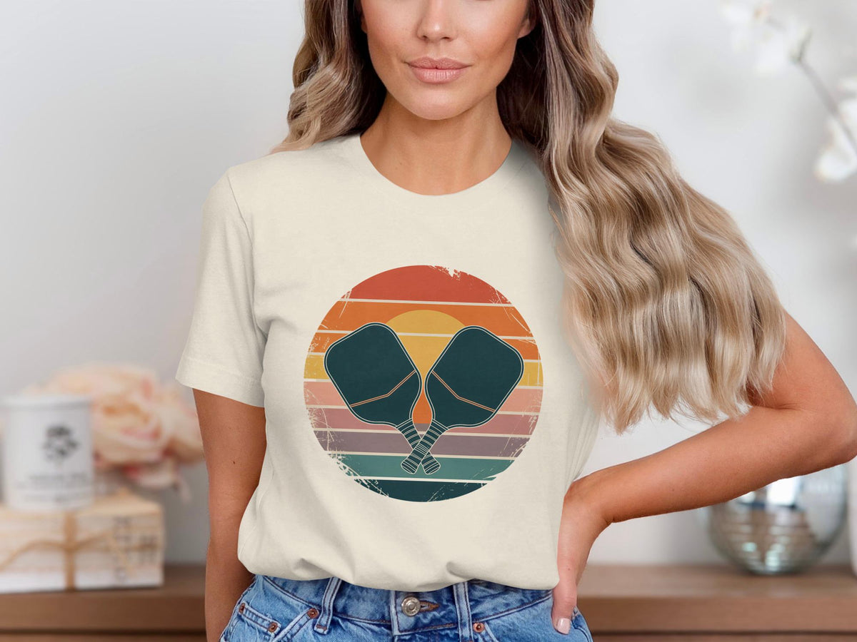 Cream t-shirt with crossed pickleball paddles in a retro sunset graphic.