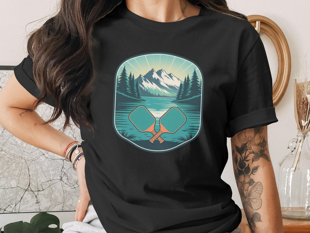 Black t-shirt with a graphic of crossed pickleball paddles and a mountain lake scene.