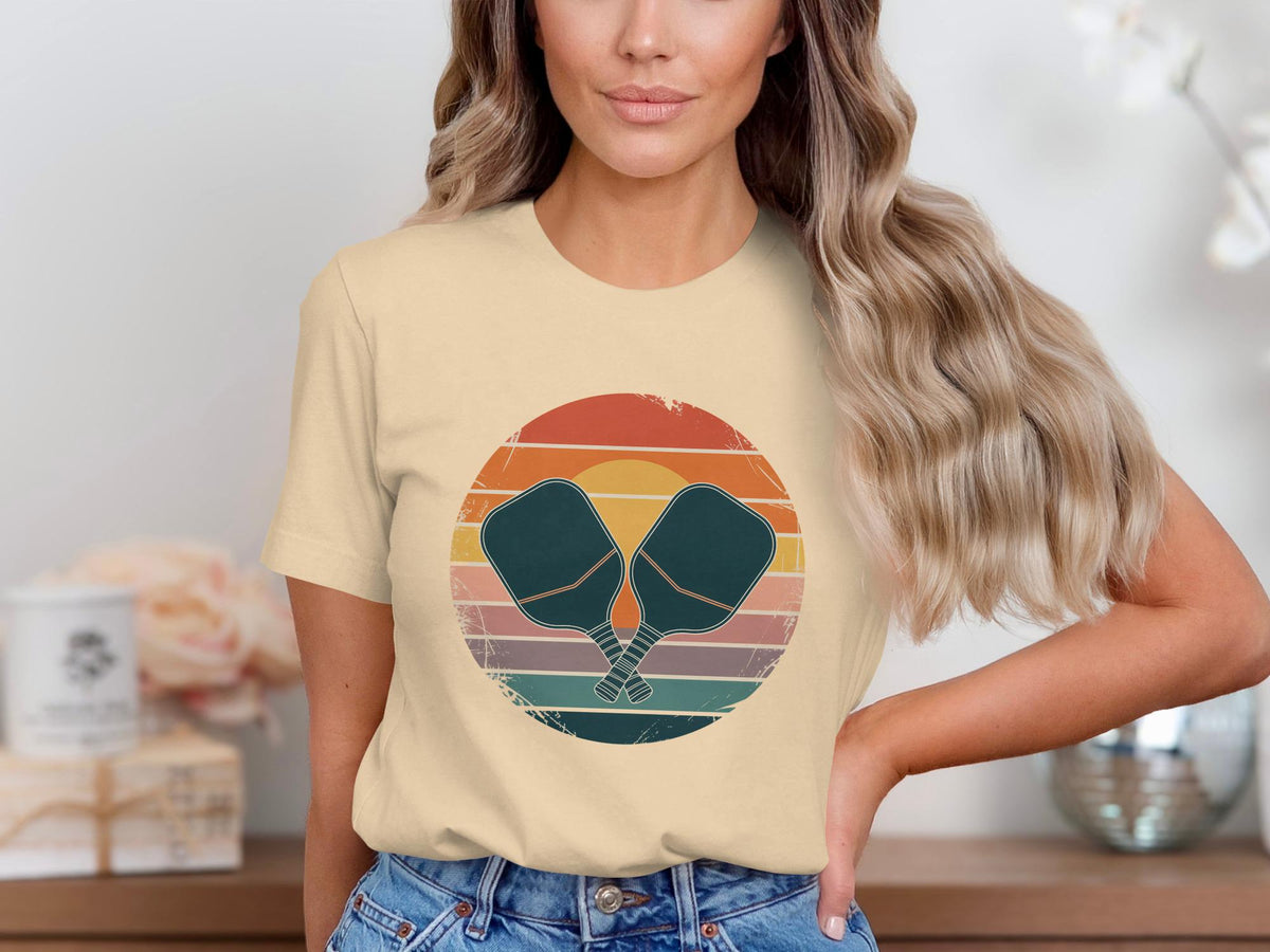Peach t-shirt with vintage sunset graphic and crossed pickleball paddles.