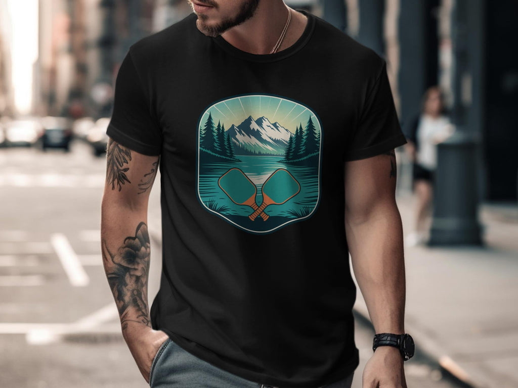 Black t-shirt with a graphic of mountains, lake, trees, and crossed pickleball paddles.