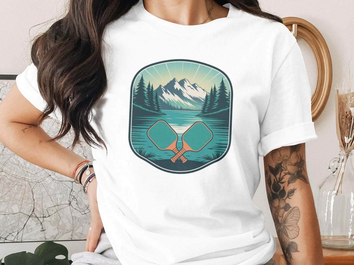 T-shirt graphic of crossed pickleball paddles with mountains and lake scene.